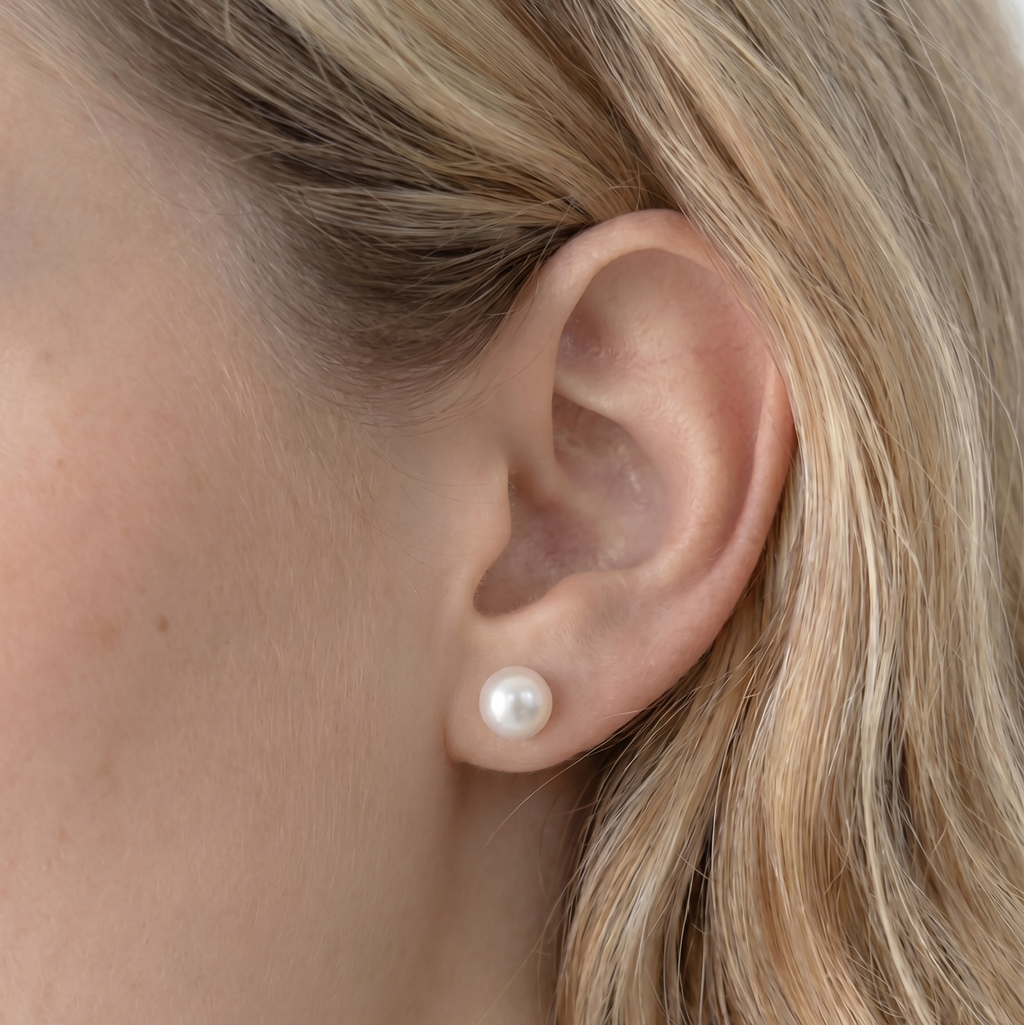 Close-up of an ear wearing a pearl earring with blonde hair.