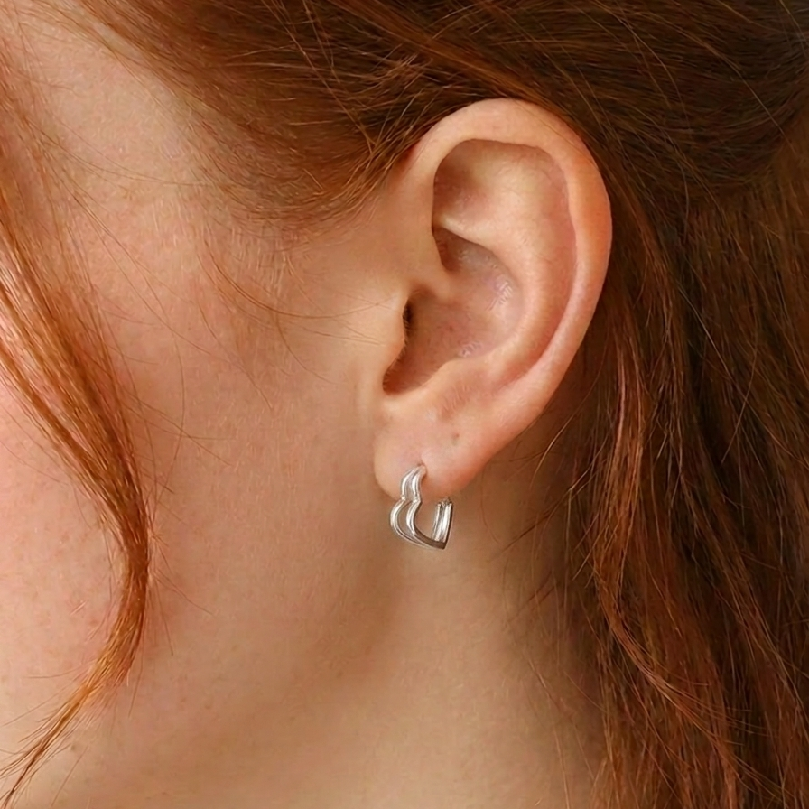 Close-up of a person wearing a silver heart-shaped earring 