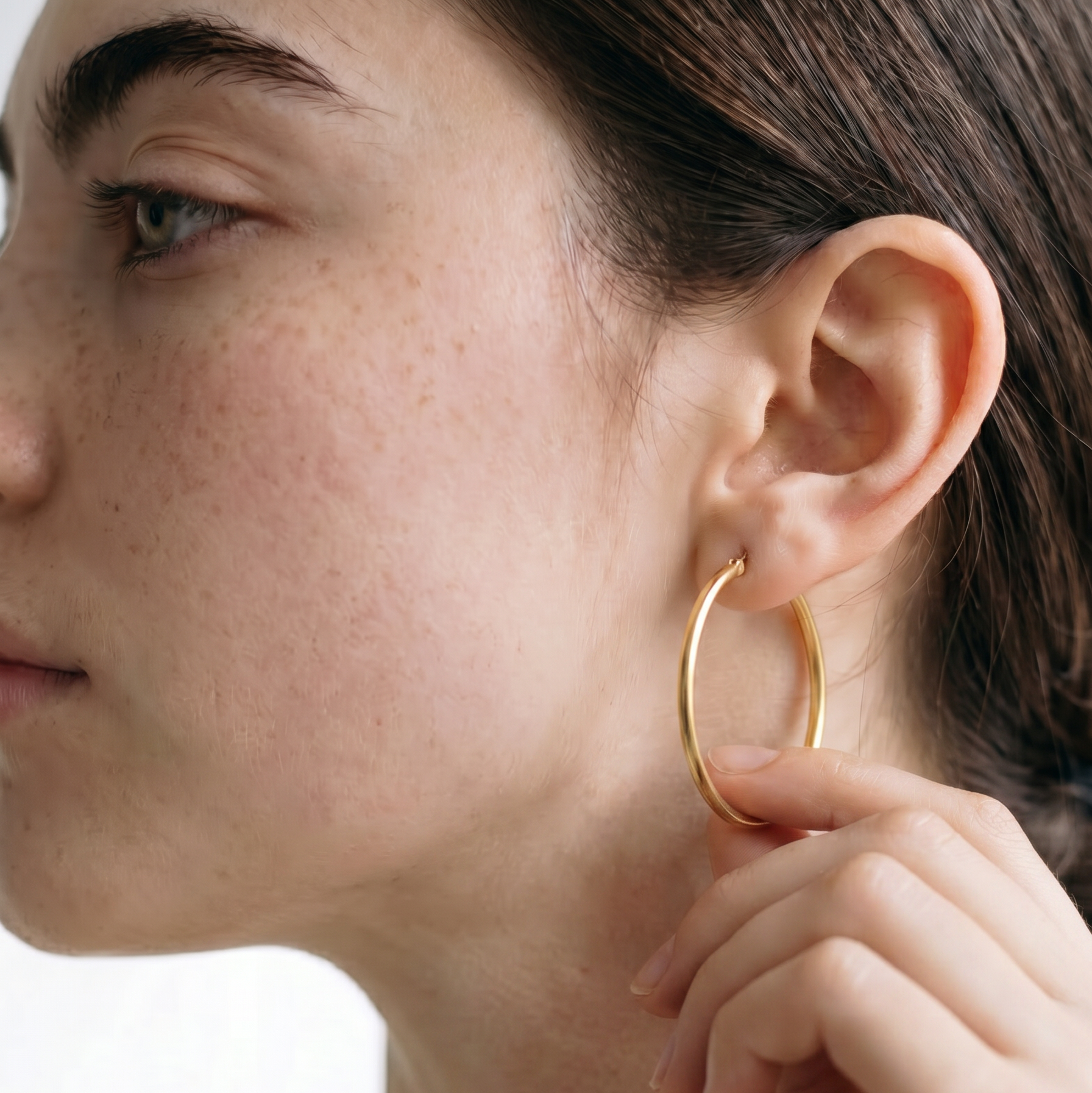 Close-up of a person wearing a gold hoop earring on a white background