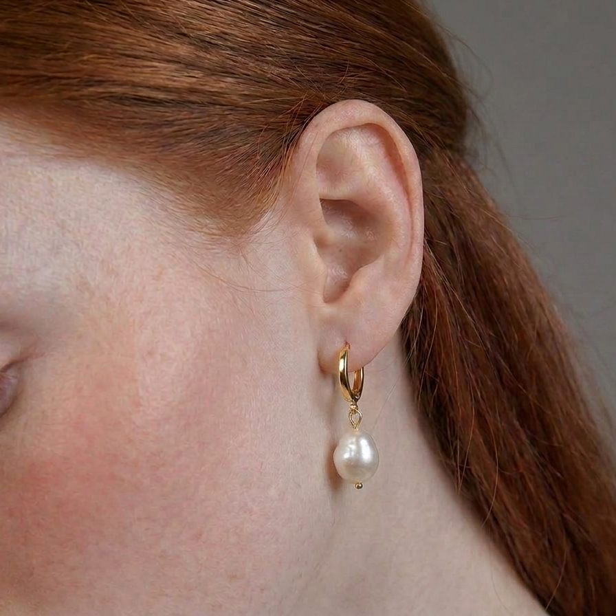 Close-up of an ear wearing a gold earring with a pearl drop.
