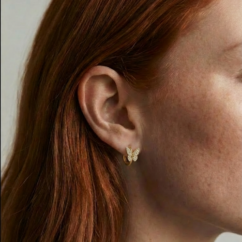 Close-up of a person wearing a gold butterfly earring with a plain background