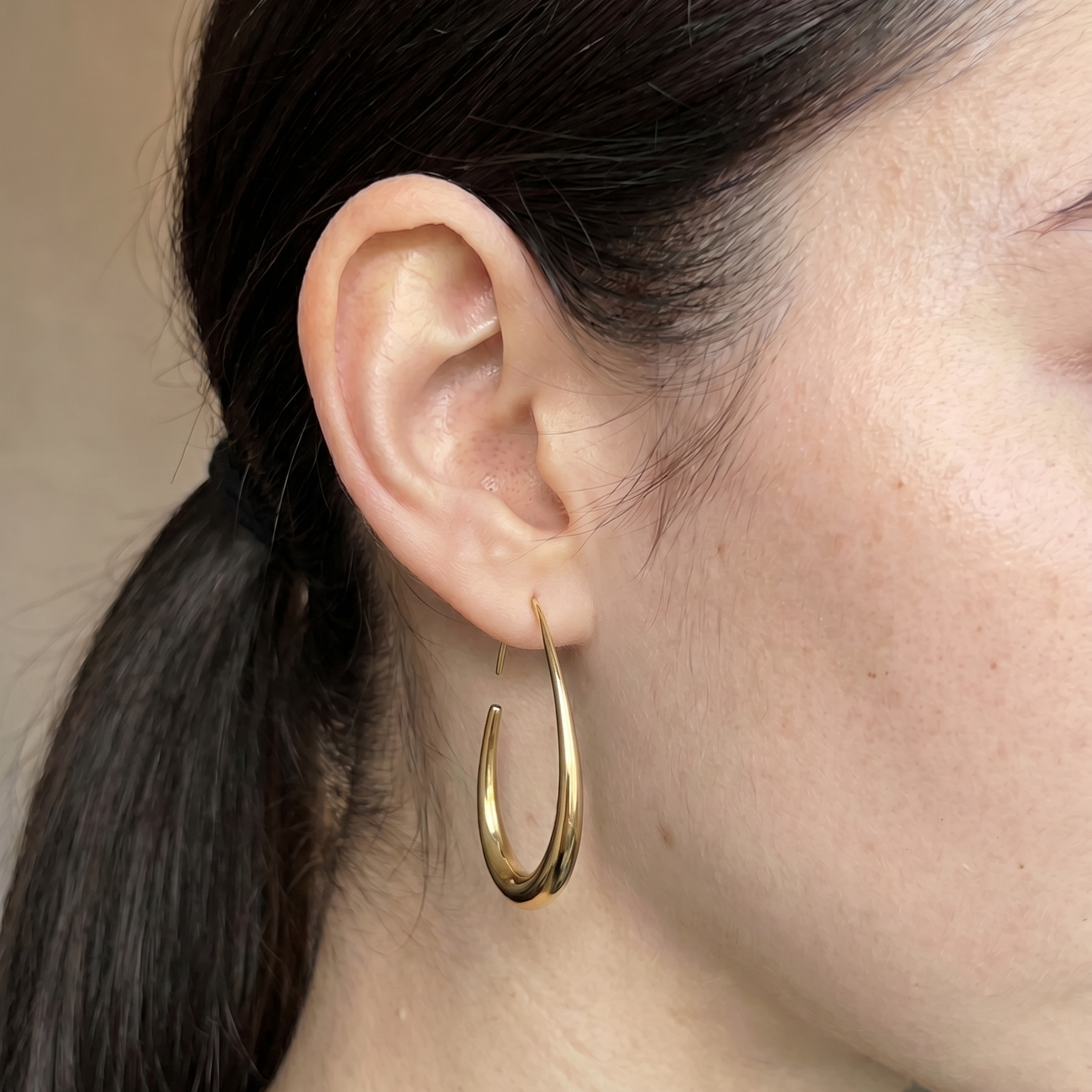 Gold hoop earring worn by a woman with dark hair.